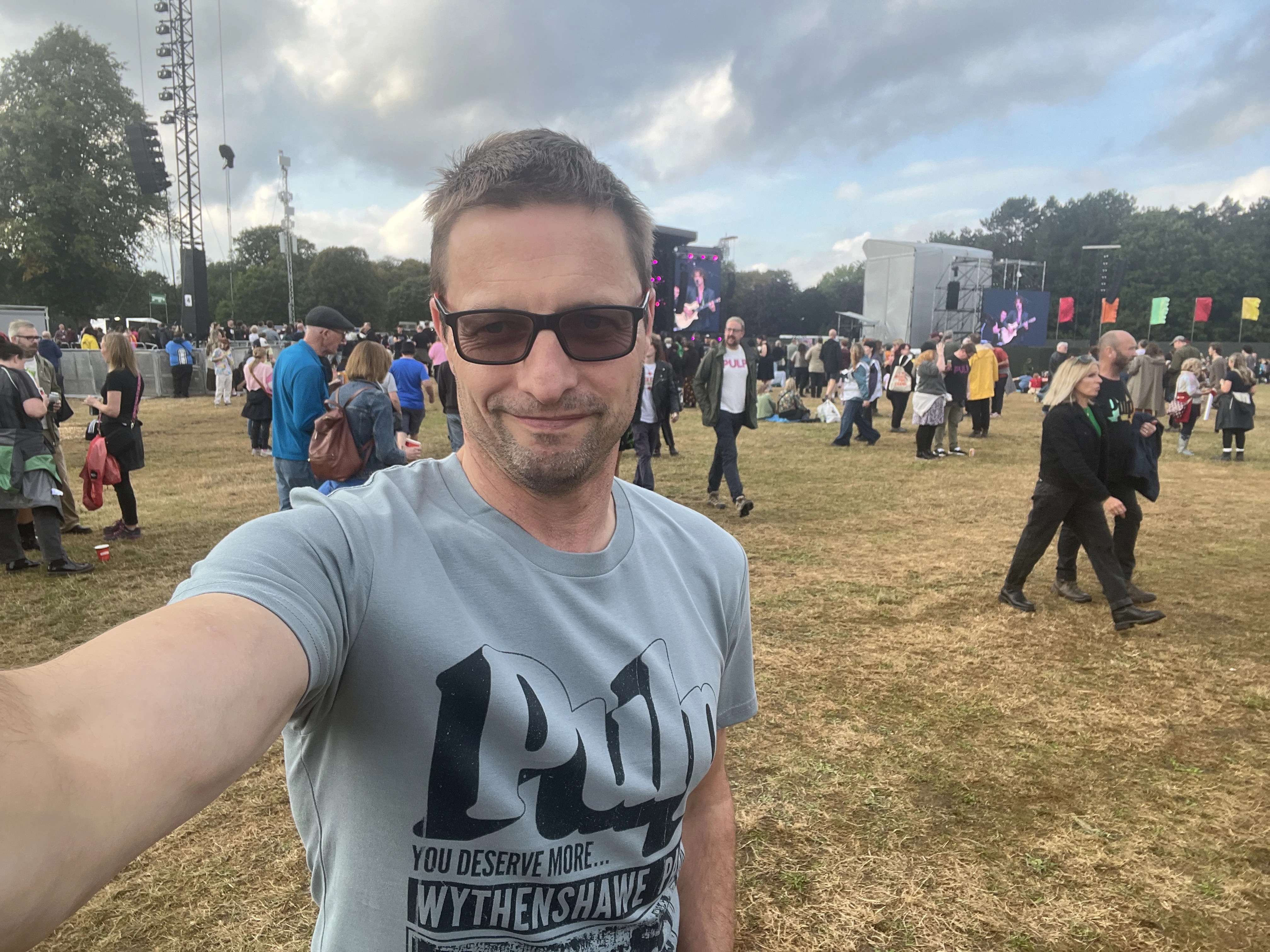 A picture of a person wearing a Pulp tee shirt, with a festival stage area beyond