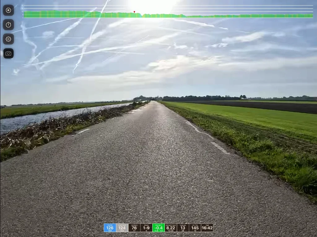 Straight rural road stretching toward distant horizon with water canal on left, green fields on right, and contrails visible in cloudy sky above.