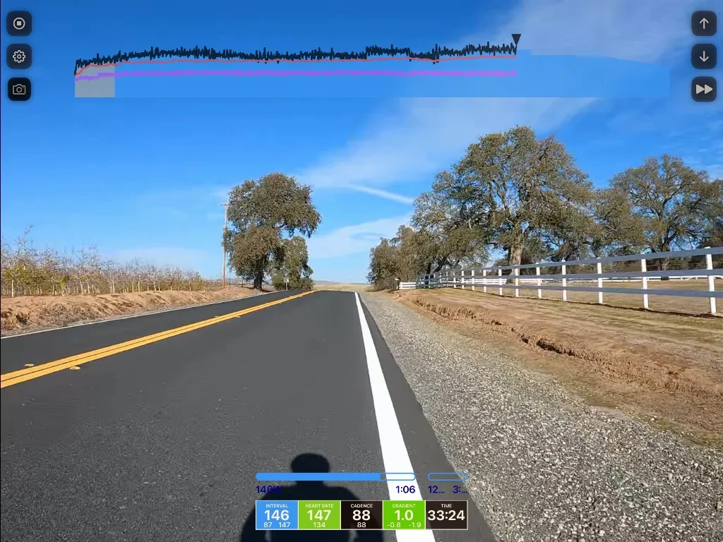 Straight rural road with yellow center line, scattered oak trees, white ranch fencing on right, brown fields, blue sky with waveform audio editor overlay and playback controls.