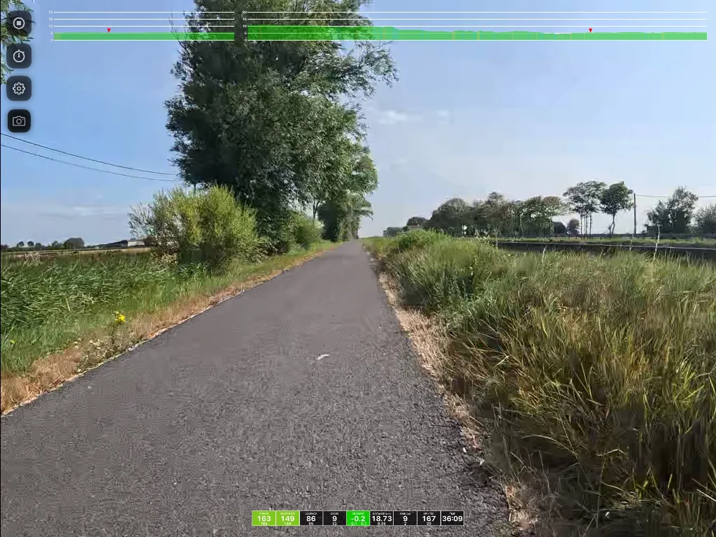 A straight rural asphalt path bordered by green fields and trees under blue sky, with cycling data displayed at bottom.