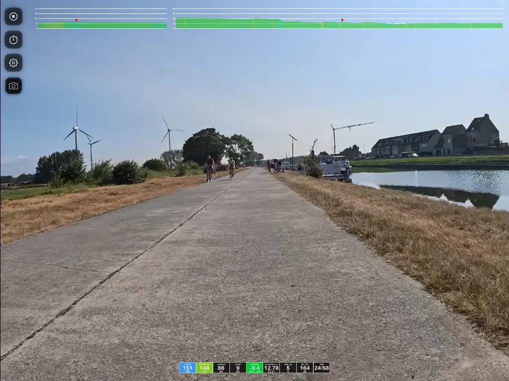 A straight paved path through flat countryside with wind turbines on the left, a canal on the right, and a large house in the distance.