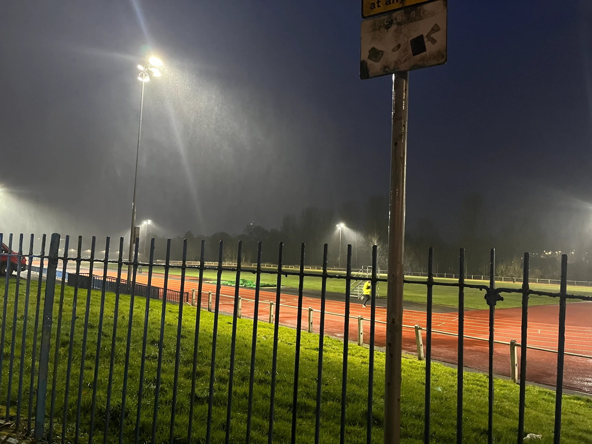 View across a running track through floodlight illuminated heavy rain