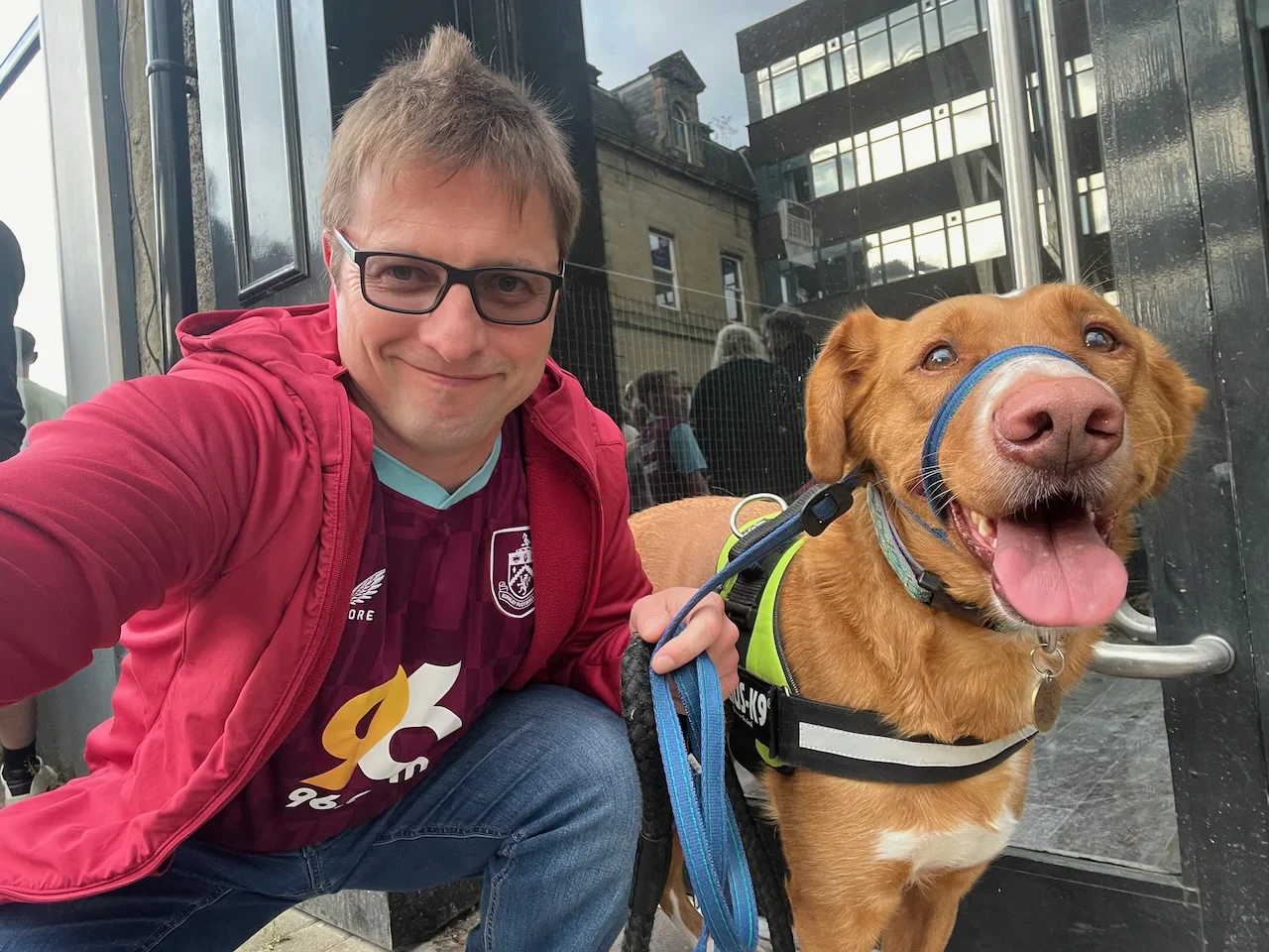 A human dressed in claret and blue with a crazy looking big ginger dog. The human looks less sane still
